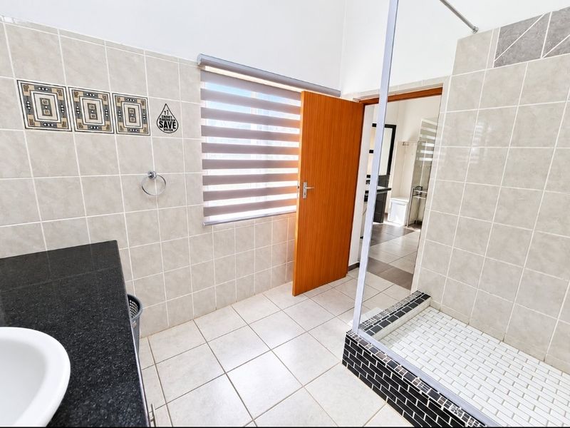 A clean, modern bathroom featuring a granite-topped vanity, tiled walk-in shower with glass enclosure, and neutral ceramic finishes throughout.