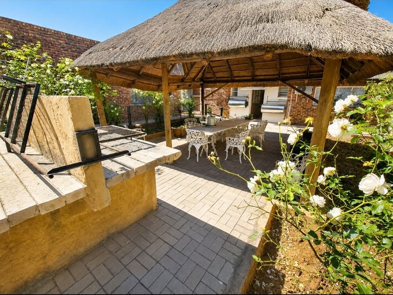 Outdoor entertainment area featuring a thatched lapa, built-in braai, and paved flooring, set within a private garden space.