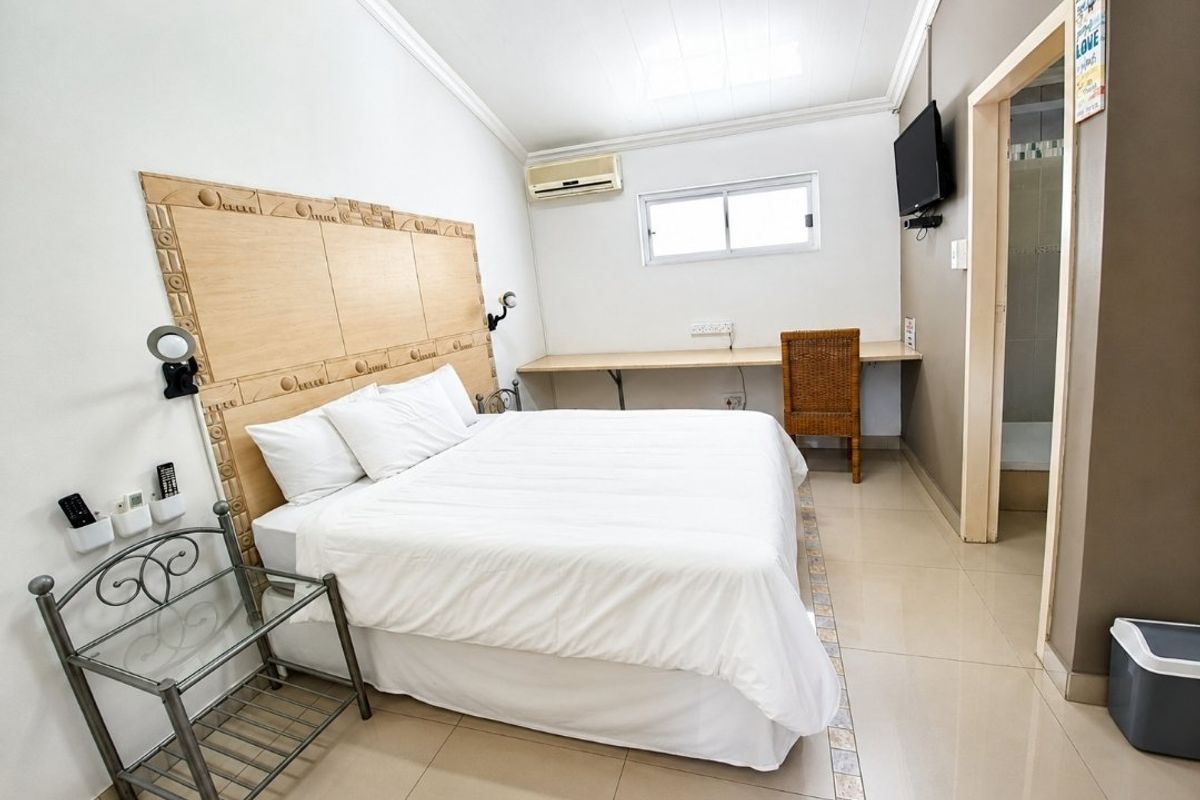 A functional bedroom featuring a built-in headboard, integrated desk space, tiled flooring, and an en-suite bathroom, offering a practical layout for guests.