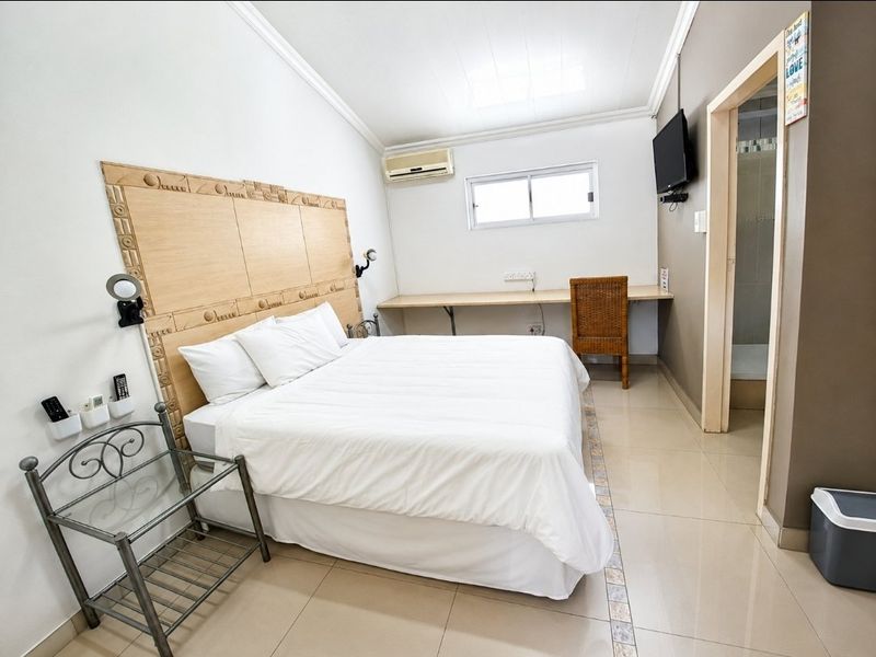 A functional bedroom featuring a built-in headboard, integrated desk space, tiled flooring, and an en-suite bathroom, offering a practical layout for guests.