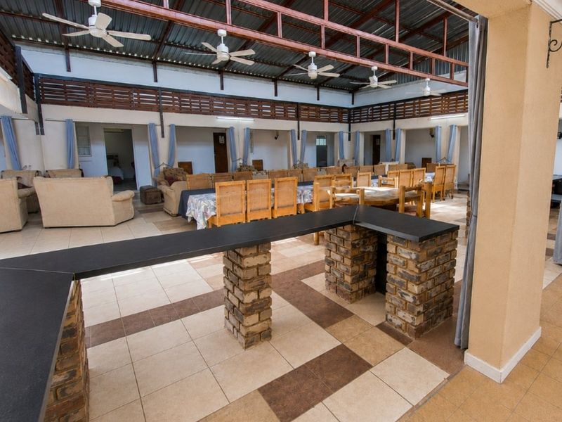 Spacious covered outdoor entertainment area featuring a brick bar counter, exposed steel roof trusses, ceiling fans, and tiled flooring.