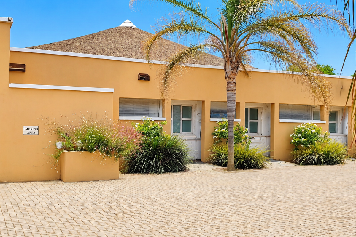 Exterior view of a commercial building featuring a thatched roof, paved courtyard, and built-in planter boxes with established landscaping.