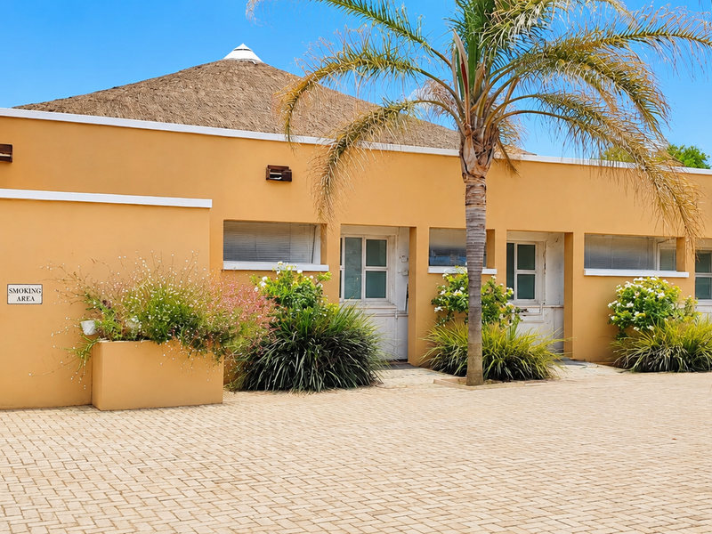 Exterior view of a commercial building featuring a thatched roof, paved courtyard, and built-in planter boxes with established landscaping.