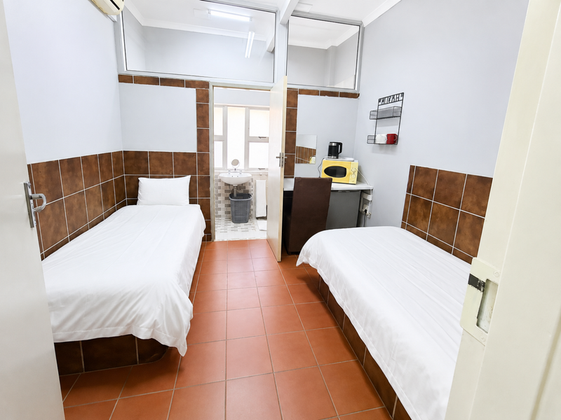 A compact bedroom featuring twin beds, tiled flooring, and a small built-in vanity area with an adjoining bathroom.