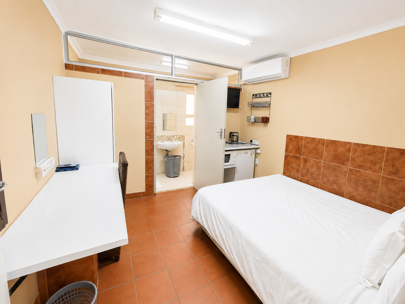 A functional bedroom featuring tiled flooring, a built-in desk, an en-suite bathroom, and an integrated air conditioning unit.