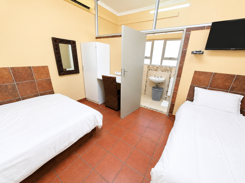 A commercial bedroom featuring tiled flooring, an en-suite bathroom with a pedestal basin, and a wall-mounted air conditioning unit.