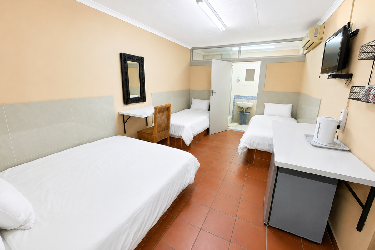 A functional commercial bedroom featuring tiled flooring, wall-mounted air conditioning, and an integrated en-suite bathroom with basic fixtures.