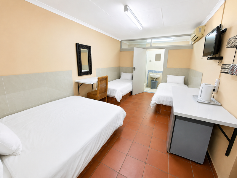 A functional commercial bedroom featuring tiled flooring, wall-mounted air conditioning, and an integrated en-suite bathroom with basic fixtures.