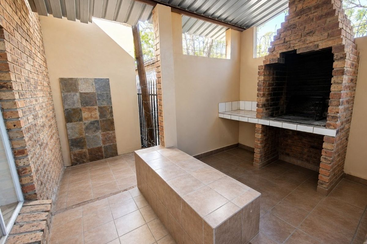 Covered outdoor entertainment area featuring a built-in brick braai, tiled preparation counter, and durable tiled flooring.