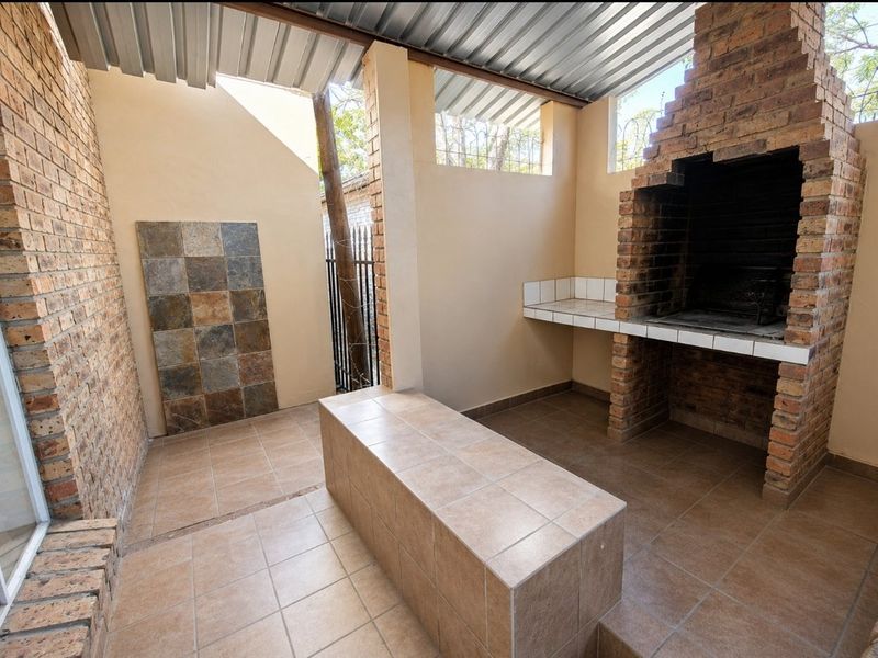 Covered outdoor entertainment area featuring a built-in brick braai, tiled preparation counter, and durable tiled flooring.