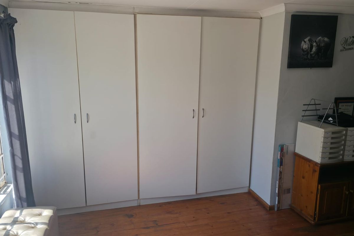 A bedroom featuring built-in cupboards and timber flooring, providing functional storage space and natural light from the adjacent window.