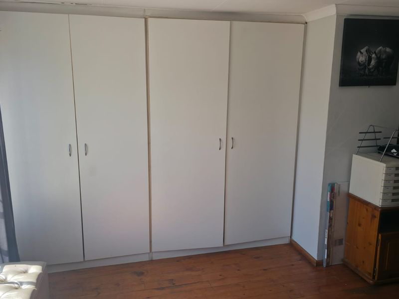 A bedroom featuring built-in cupboards and timber flooring, providing functional storage space and natural light from the adjacent window.