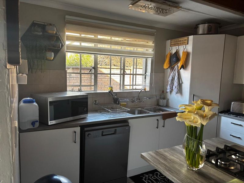 A functional kitchen featuring white cabinetry, laminate countertops, a double sink, and a built-in gas hob, offering a practical layout for daily meal preparation.