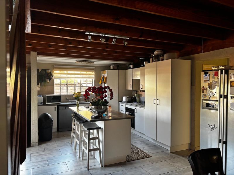 A functional kitchen featuring a central island, white cabinetry, and exposed timber ceiling beams, providing a warm and practical cooking space.