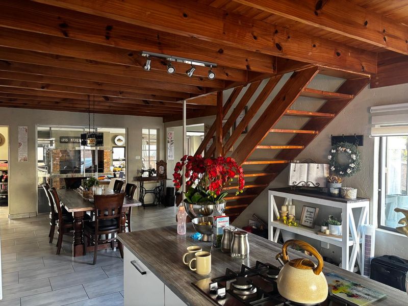 Spacious open-plan living area featuring exposed timber ceiling beams, a wooden staircase, and a modern kitchen island with a built-in gas hob.