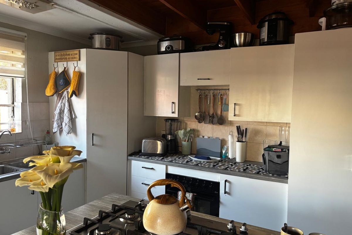 A functional kitchen featuring white cabinetry, a gas hob, built-in oven, tiled backsplash, and exposed timber ceiling beams.