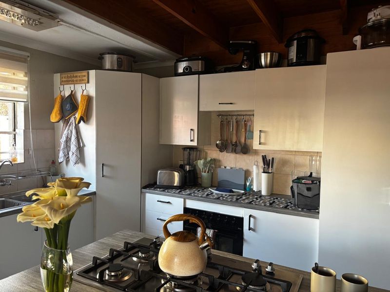 A functional kitchen featuring white cabinetry, a gas hob, built-in oven, tiled backsplash, and exposed timber ceiling beams.