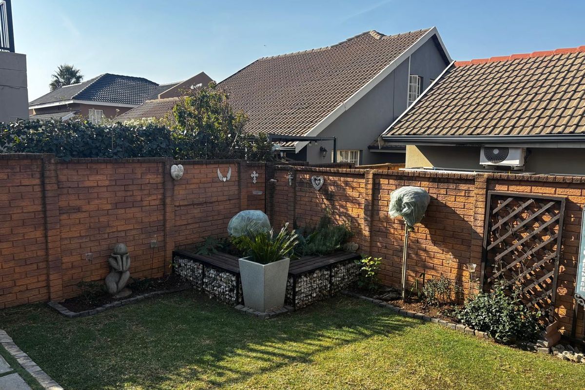 A private rear garden featuring a well-maintained lawn, brick boundary walls, and a decorative gabion planter box.