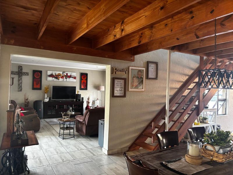 Open-plan living area featuring exposed timber ceiling beams, a wooden staircase, and tiled flooring, creating a warm and connected living and dining space.