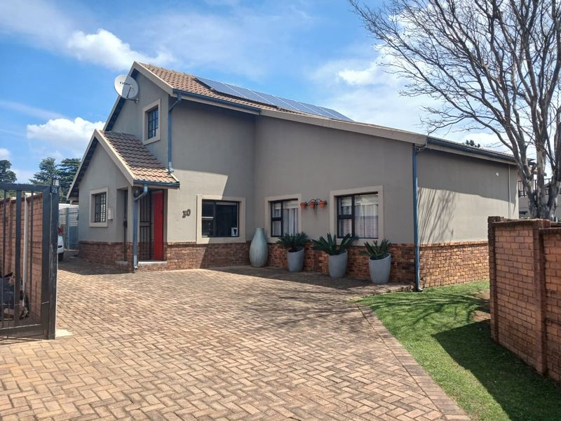 Front exterior view of a townhouse featuring a brick paved driveway, tiled roof, solar panels, and secure perimeter walling.