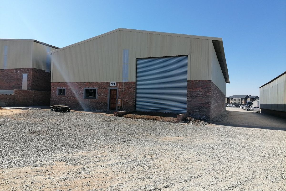 Industrial warehouse unit featuring a large roller shutter door, brick and metal cladding exterior, and a spacious gravel yard area.