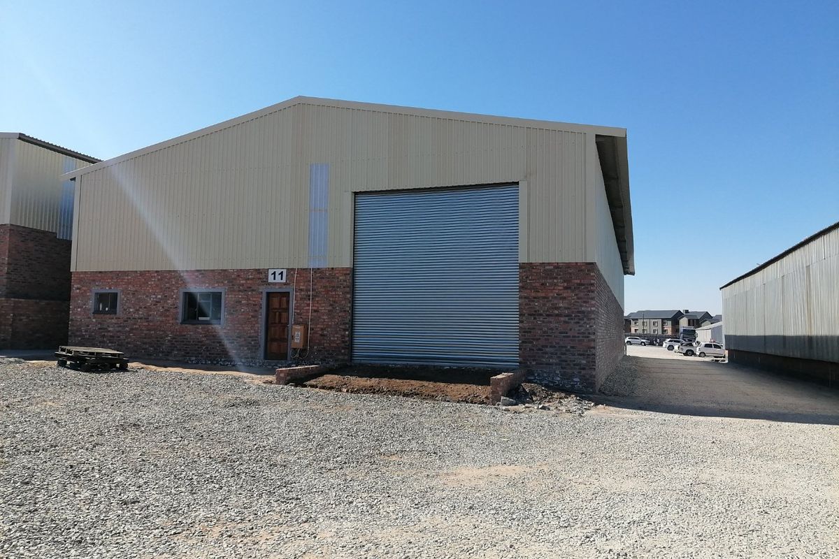 Industrial warehouse unit featuring a large roller shutter door, brick and metal cladding exterior, and a gabled roof design.