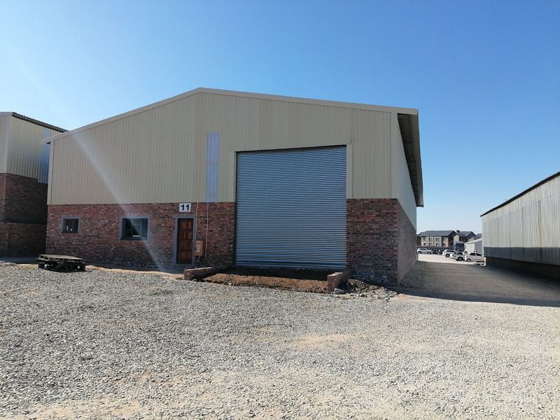 Industrial warehouse unit featuring a large roller shutter door, brick and metal cladding exterior, and a gabled roof design.