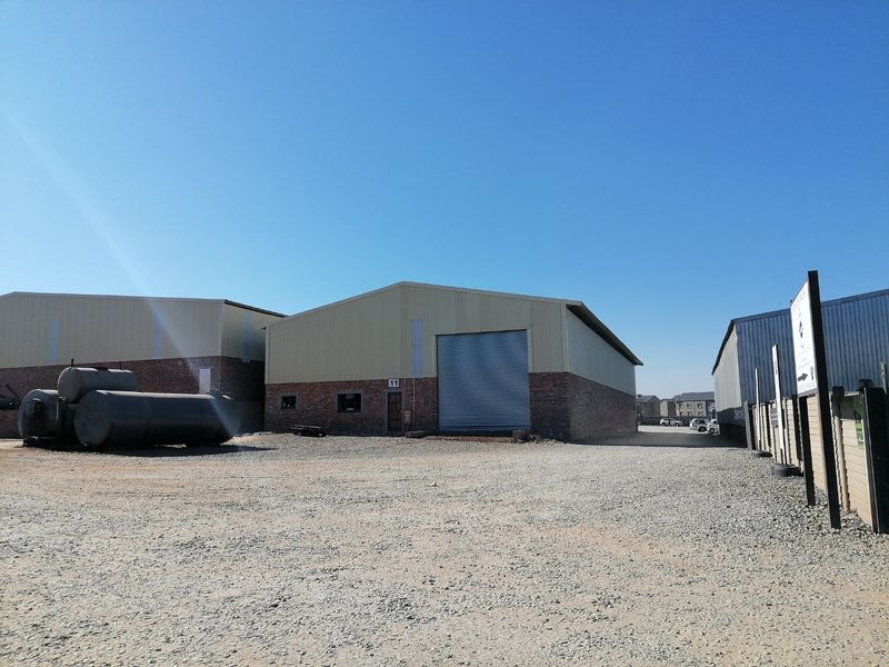 Industrial warehouse unit featuring a brick and metal facade, large roller shutter door, and a spacious gravel yard area.