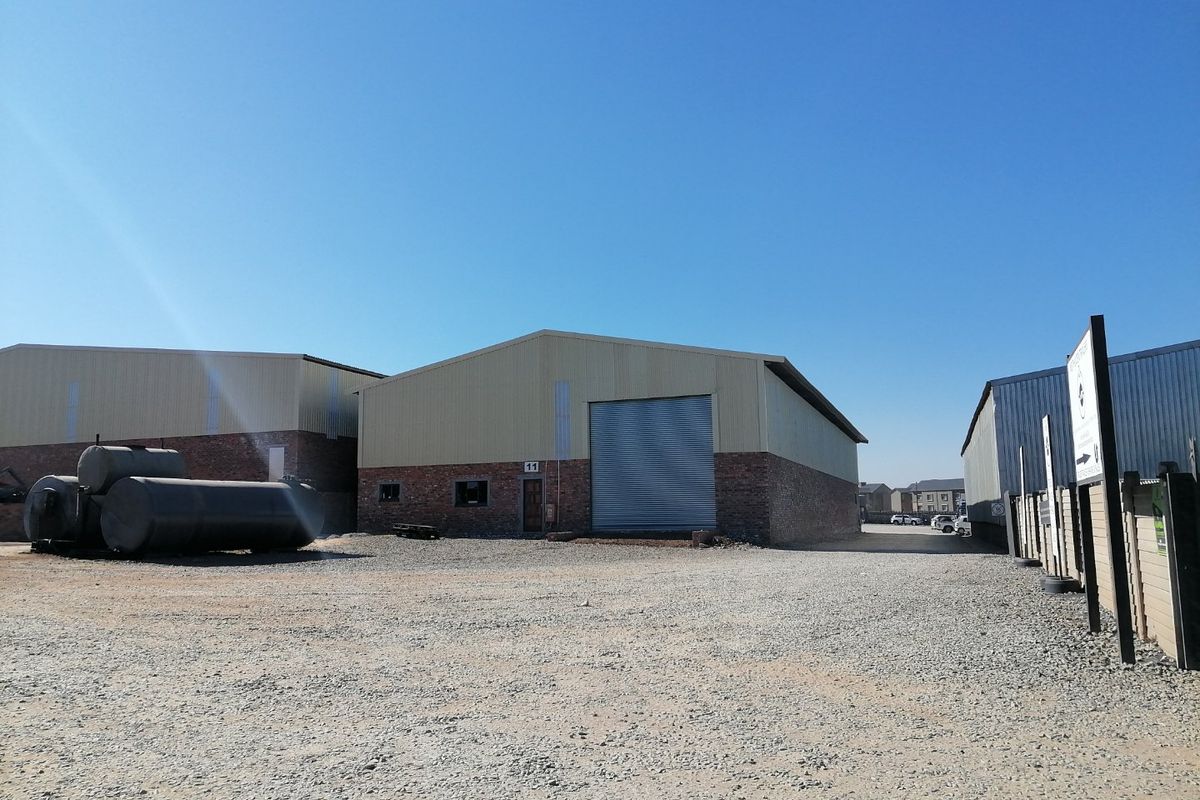 Industrial warehouse unit featuring a brick and metal facade, large roller shutter door, and a spacious gravel yard area.