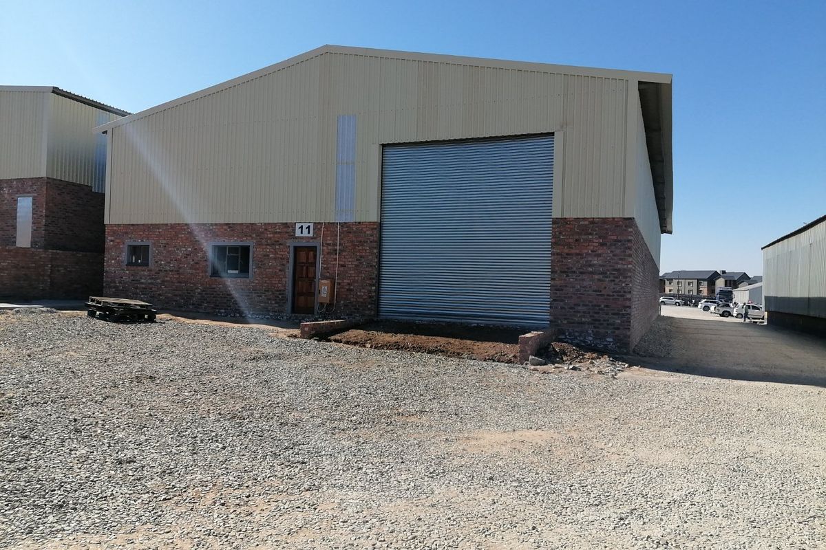 Industrial warehouse unit featuring a large roller shutter door, brick and metal cladding exterior, and a gravel yard area.