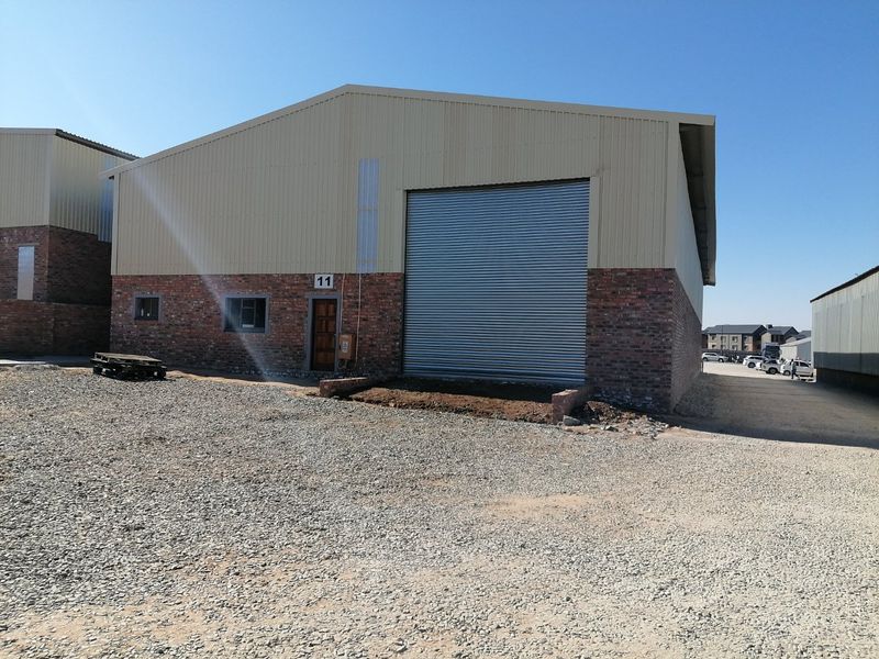 Industrial warehouse unit featuring a large roller shutter door, brick and metal cladding exterior, and a gravel yard area.
