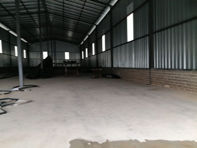 Spacious industrial warehouse unit featuring high ceilings, corrugated metal walls, and a durable concrete floor, suitable for storage or manufacturing operations.