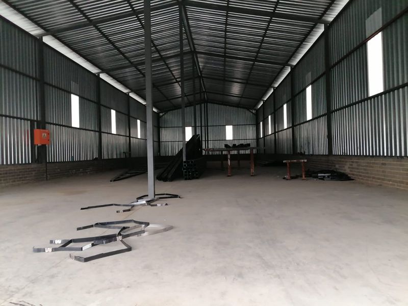 Spacious industrial warehouse unit featuring high ceilings, corrugated metal walls, and a durable concrete floor, suitable for storage or manufacturing operations.