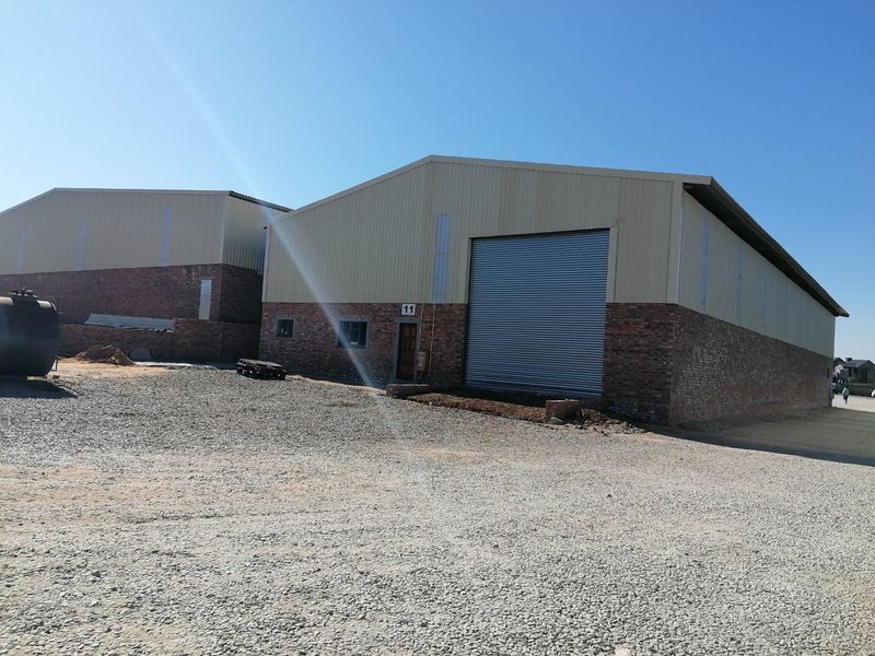 Industrial warehouse unit featuring a brick and metal facade, large roller shutter door, and an expansive gravel yard area.