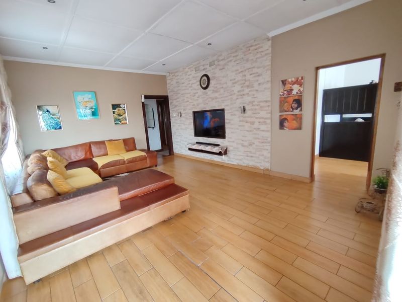 A spacious living room featuring wood-look tiled flooring, a textured stone-cladding feature wall with a built-in television niche, and recessed ceiling lighting.