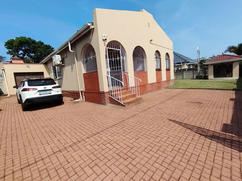 Front exterior view of the house featuring brick paving, arched windows with security gates, and an attached garage.