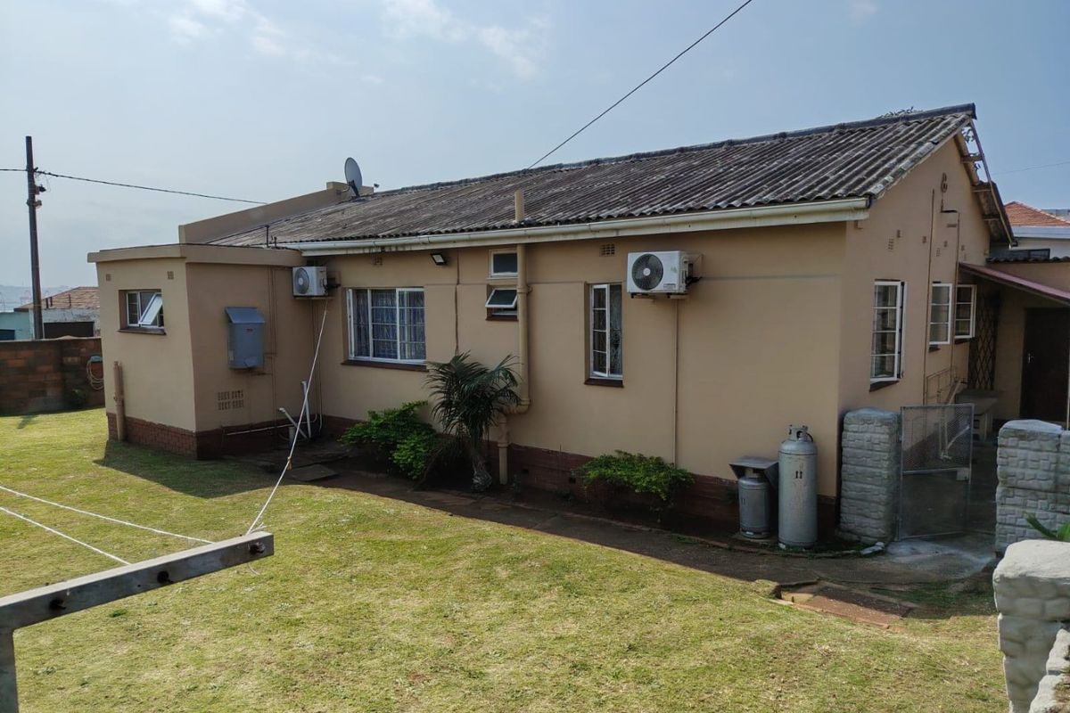 Rear view of the property featuring a tiled roof, exterior air conditioning units, and a private garden area.