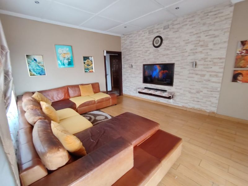 A living room featuring laminate flooring, a textured brick-style feature wall, and recessed ceiling lighting.