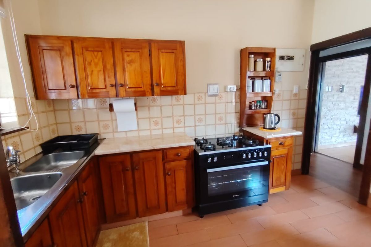A functional kitchen featuring wooden cabinetry, a double basin sink, tiled backsplash, and a freestanding gas stove with oven.
