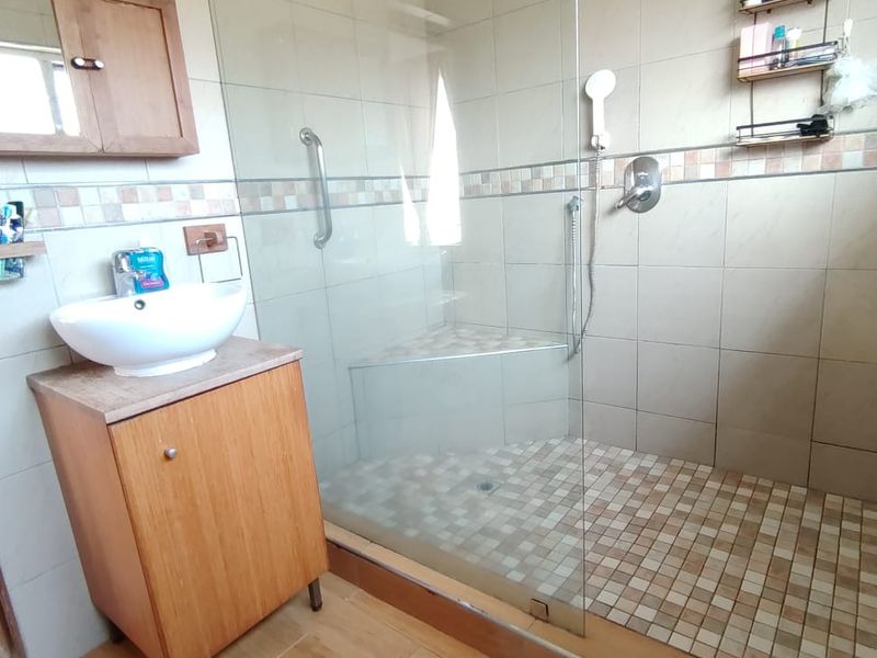 A functional bathroom featuring a walk-in shower with a glass screen, built-in shower seat, and a modern vessel sink vanity unit.