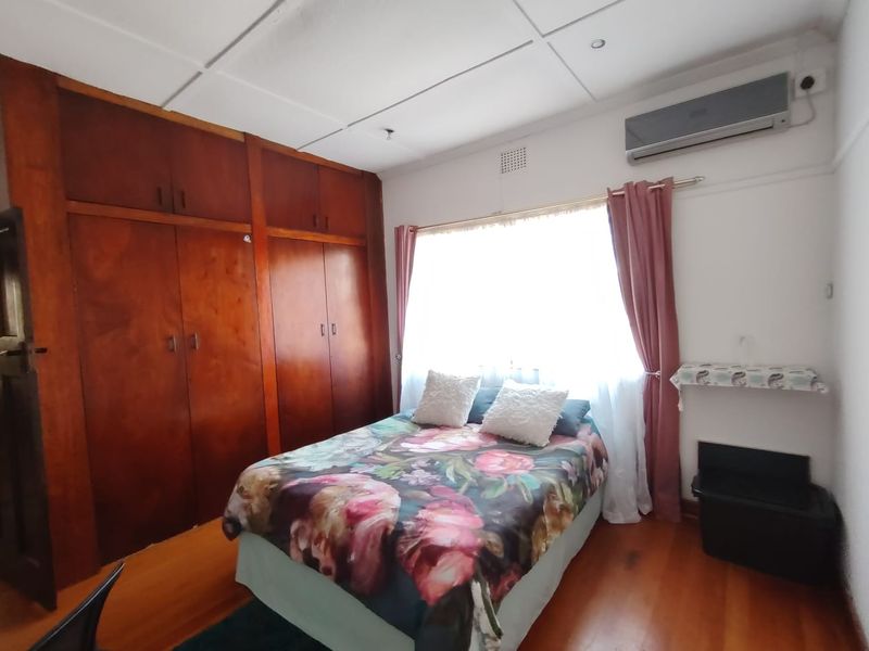 A bedroom featuring timber flooring, built-in wooden cupboards, and a wall-mounted air conditioning unit.
