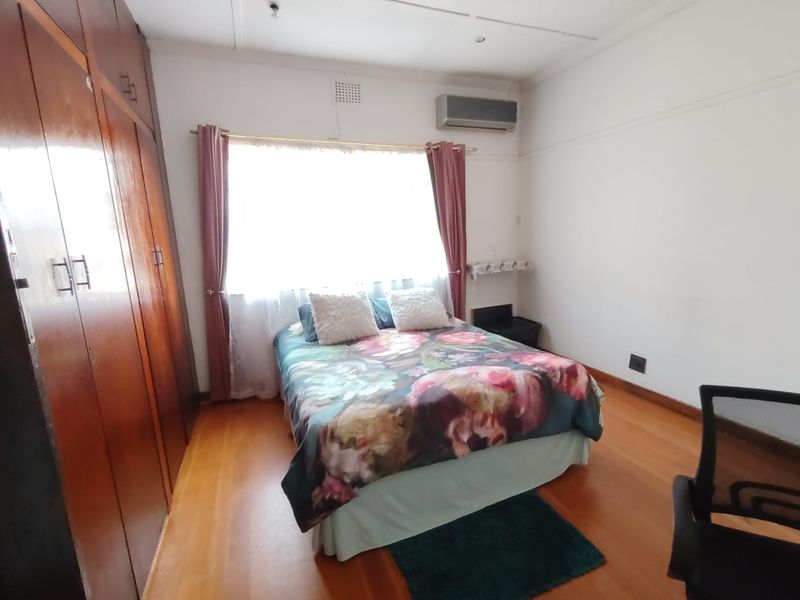A bedroom featuring wooden flooring, built-in cupboards, and an air conditioning unit.