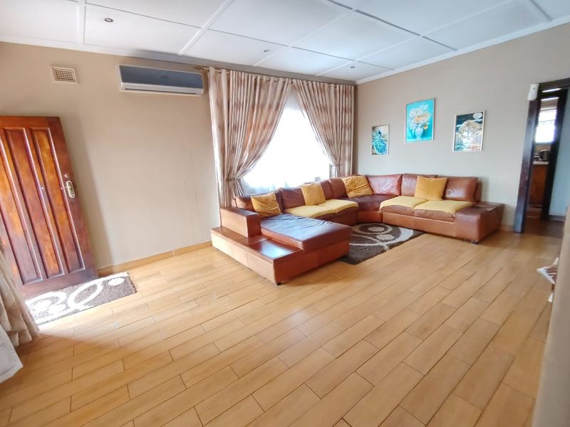A spacious living room featuring timber flooring, a split-system air conditioner, and a tiled ceiling, offering a comfortable and functional living space.