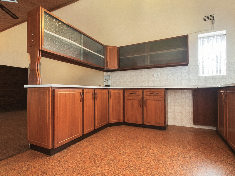 A spacious, dated kitchen featuring extensive wooden cabinetry, tiled backsplash, and traditional tiled flooring, offering significant potential for a modern renovation.