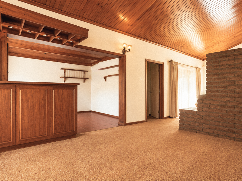 A spacious living area featuring a built-in wooden bar, vaulted timber ceiling, and a prominent exposed brick fireplace.
