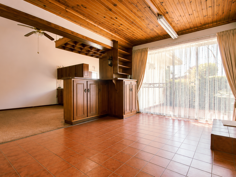 Spacious open-plan living area featuring a built-in timber bar, tiled flooring, and large sliding glass doors leading to the exterior.