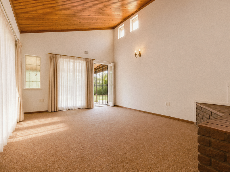 Spacious living area featuring a high timber raked ceiling, carpeted flooring, and a built-in brick fireplace hearth with direct access to the outdoor area.