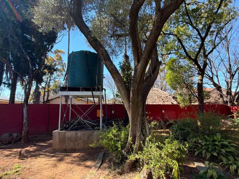A garden area featuring a large water storage tank mounted on a raised metal stand with a concrete base and perimeter walling.