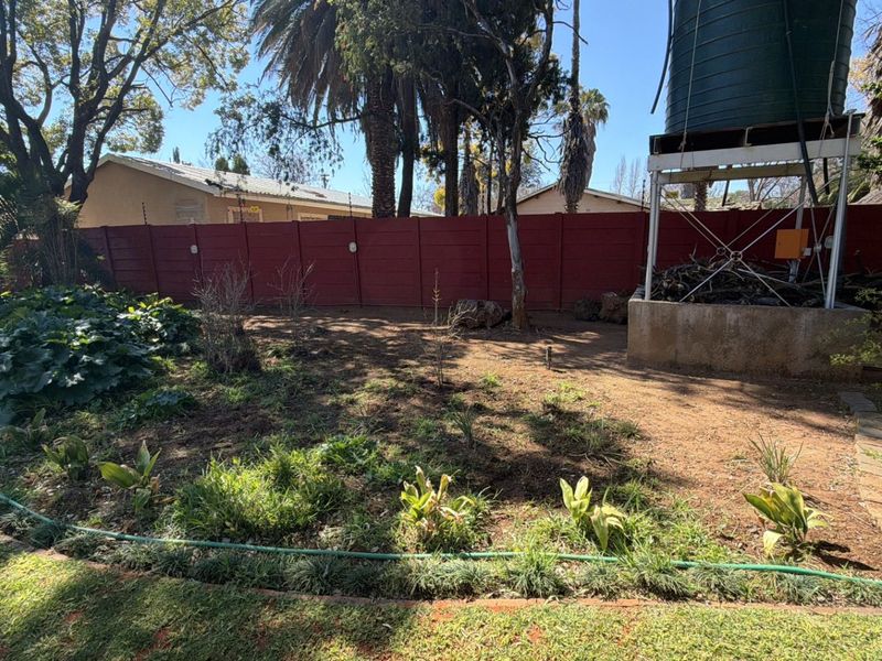 A rear garden area featuring a water tank on a raised stand, enclosed by a red precast concrete wall with electric fencing.