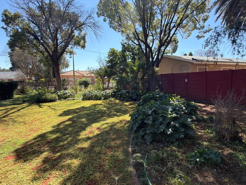 A spacious residential garden featuring established trees, lawn area, and perimeter fencing.